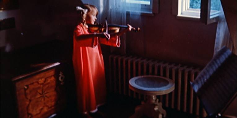 Ein Mädchen in einem langen roten Nachthemd steht am Fenster und spielt auf einer Geige.